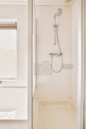 Photo for A bathroom with a bathtub, shower head and handrails on the wall in front of the tub - Royalty Free Image