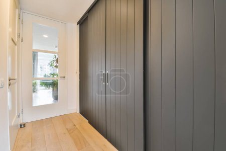 un pasillo con suelos de madera y paneles de pared pintados de gris en las paredes, que conduce a una entrada