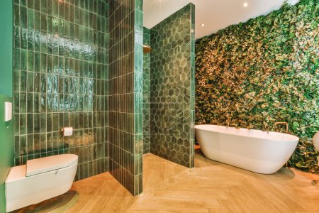 Téléchargez les photos : Une salle de bain avec des carreaux verts sur les murs et du parquet autour de la baignoire, des toilettes et de la baignoire - en image libre de droit