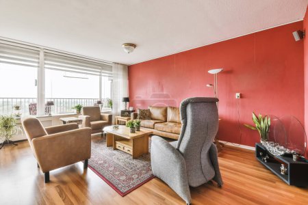 Foto de Una sala de estar con paredes rojas y pisos de madera, dos sillas y una mesa de café en la parte media de la habitación - Imagen libre de derechos