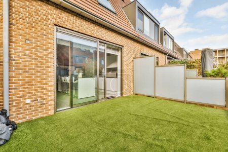 Photo for An outside area with green grass and brick buildings in the background, including a sliding glass door that leads to a patio - Royalty Free Image