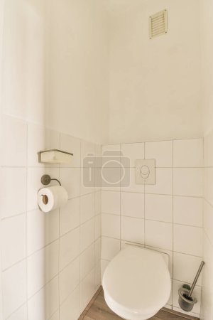 Photo for A white toilet in a small bathroom with wood flooring and tile on the walls there is a trash can be seen - Royalty Free Image