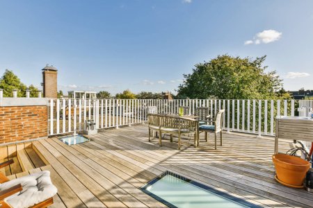 Photo for A wooden deck with chairs and an outdoor pool in the middle part of the deck, surrounded by white pickets - Royalty Free Image