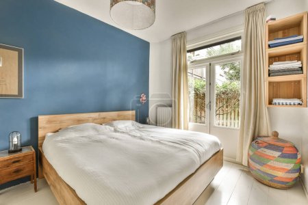 Téléchargez les photos : Une chambre avec des murs bleus et un plancher blanc, des têtes de lit en bois et un lit devant une fenêtre - en image libre de droit