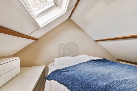 Téléchargez les photos : Un lit dans une chambre avec des murs blancs et des garnitures en bois autour des têtes de lit, sous une lucarne - en image libre de droit