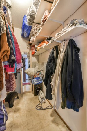 The inside of a closet with clothes hanging on hooks, and other items in storage space around it to be used