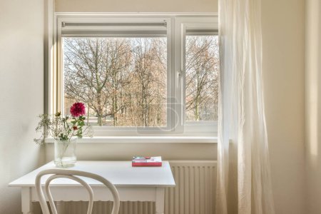 Téléchargez les photos : Une chambre avec une fenêtre, une table et des fleurs sur les appuis des fenêtres devant la fenêtre sont des arbres nus - en image libre de droit