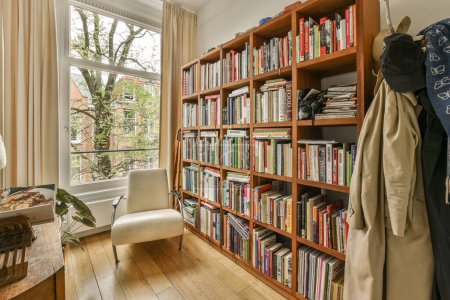 Foto de Una sala de estar con libros en los estantes y una silla frente a una estantería llena de libros - Imagen libre de derechos