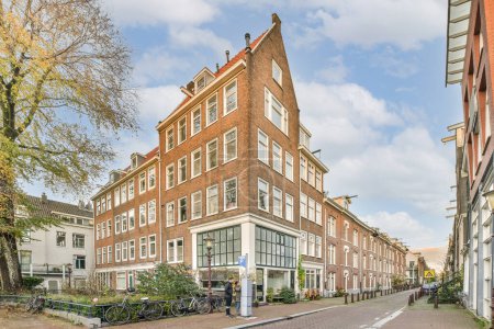 Amsterdam, Netherlands - 10 April, 2021: a city street with buildings and bicycles parked on the side of the road in front of it, there is a cloudy blue sky