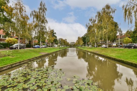 Téléchargez les photos : Amsterdam, Pays-Bas - 10 avril 2021 : un canal avec des nénuphars à l'avant et des maisons de l'autre côté, le tout entouré d'arbres feuillus - en image libre de droit