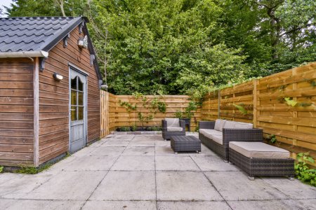 Téléchargez les photos : Amsterdam, Pays-Bas - 10 Avril, 2021 : une zone arrière-cour avec des clôtures en bois et des meubles de jardin sur le patio, entouré d'arbres verts luxuriants en arrière-plan - en image libre de droit