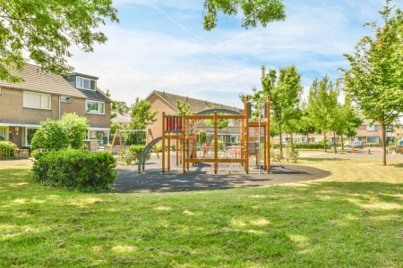 Foto de Una zona de juegos para niños en el patio trasero con algunos árboles y casas en el fondo en un día soleado - Imagen libre de derechos