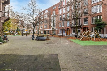 Foto de Ámsterdam, Países Bajos - 10 de abril de 2021: un parque en medio de una zona urbana con árboles, bancos y parques infantiles a ambos lados - Imagen libre de derechos