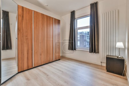 Foto de Un dormitorio con suelos de madera y paredes blancas, hay un gran espejo en la pared al lado de la cama - Imagen libre de derechos