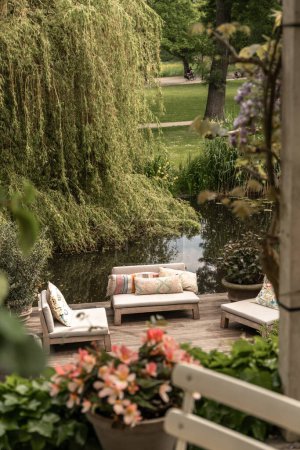 Téléchargez les photos : Un espace de vie extérieur avec des canapés, des tables et des fleurs sur le pont en arrière-plan est un grand saule - en image libre de droit