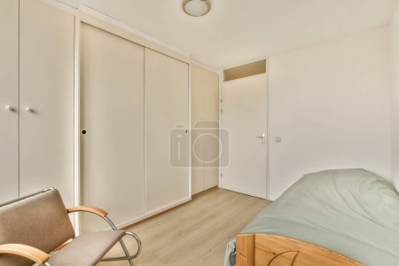 Photo for A bedroom with a bed, chair and closets on the wall to the right is an open door that leads to another room - Royalty Free Image