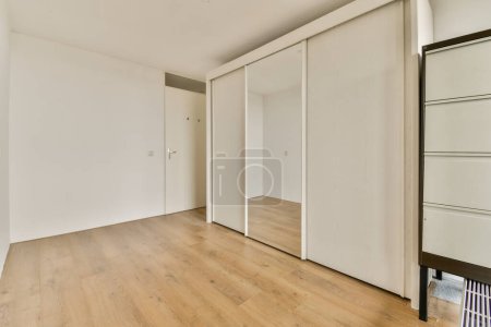 Photo for An empty room with white walls and wood flooring on the right side, there is a mirror in the corner - Royalty Free Image