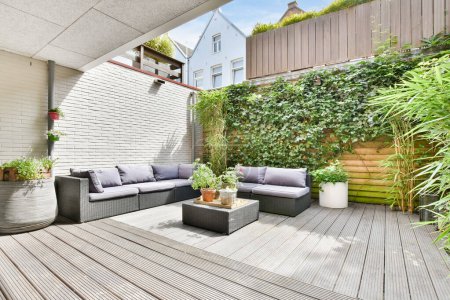 an outdoor living area with wood flooring and plants on the wall, including potted planters and sofas