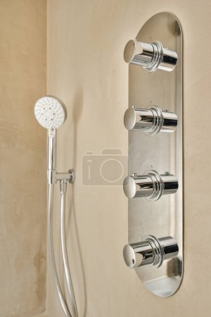 Photo for A wall mounted shower with two handsets and an overhead hand showerhead in the background is a tan colored wall - Royalty Free Image