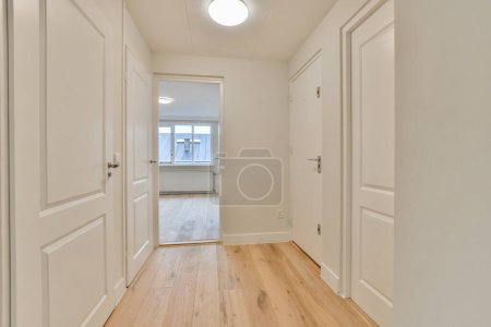 Photo for An empty room with white walls and wood flooring on the right side of the room, there is a door leading to another - Royalty Free Image