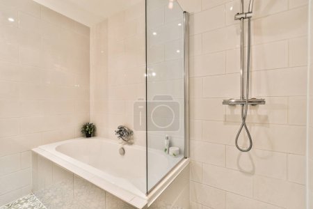Photo for A bathroom with a bathtub, shower and plant in the corner on the right hand side of the tub - Royalty Free Image