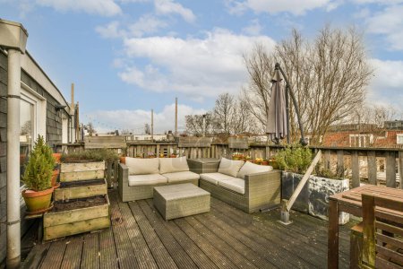 Photo for An outdoor living area with wood flooring and white couches on a wooden deck in the sky is partly blue - Royalty Free Image