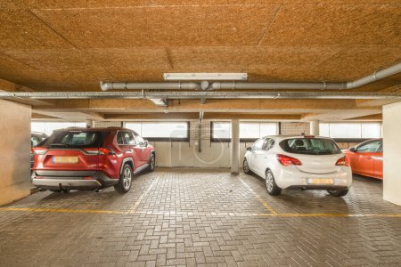 Photo for Two cars parked in an underground parking space, one is red and the other is white with yellow lines on the floor - Royalty Free Image