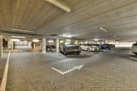 Photo for An underground parking area with cars parked in the garages and people walking on the sidewalk to get their rides - Royalty Free Image