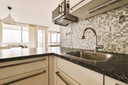 Photo for A kitchen with black and white tiles on the backs, counter tops, and sink fauced in it - Royalty Free Image