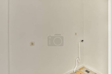 Photo for A toilet in the corner of a room with white walls and tile on the floor, there is an open door - Royalty Free Image