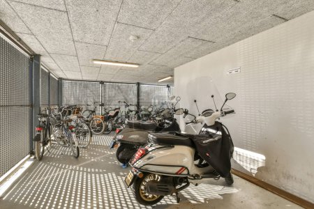 Foto de Algunas motocicletas estacionadas en una habitación con muchas bicicletas en la pared y una bicicleta está apoyada contra la pared - Imagen libre de derechos