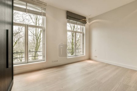 una habitación vacía con suelos de madera y grandes ventanales con vistas a los árboles en la foto se toma desde el interior