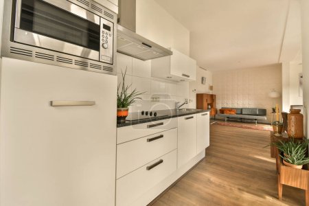 Foto de Una cocina con suelos de madera y electrodomésticos blancos en la pared, junto con una puerta abierta que conduce al salón - Imagen libre de derechos