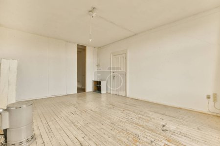 Foto de Una habitación vacía con paredes blancas y suelos de madera en un lado, hay un calentador en la esquina - Imagen libre de derechos