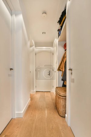Photo for A long hallway with white walls and wood flooring on the right side, there is an open door that leads to another room - Royalty Free Image