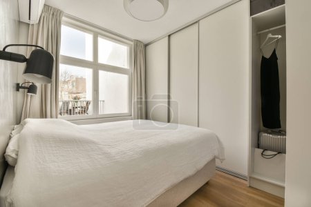 Photo for A bedroom with a bed and closets in the back ground, there is a large window that looks out onto the street - Royalty Free Image