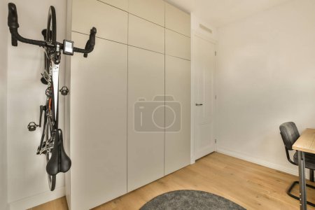 Photo for A bike hanging on the wall next to a table and chair in a room with white walls, wood floors and wooden flooring - Royalty Free Image