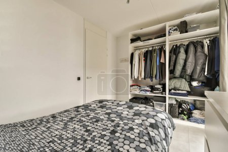 Photo for A bedroom with a bed, closets and clothes hanging on the wall next to each other room dividers - Royalty Free Image