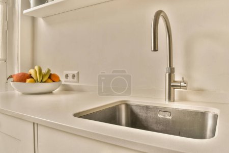 Photo for A sink and some fruit in a bowl on the kitchen counter with an open window to the wall behind it - Royalty Free Image