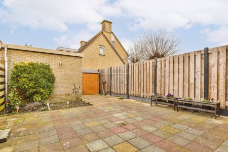 Téléchargez les photos : Une cour arrière avec des bancs et des clôtures en bois sur le côté d'une maison par une journée nuageuse de ciel bleu - en image libre de droit