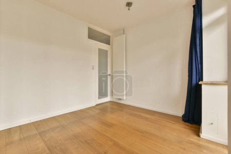 una habitación vacía con suelos de madera y cortinas azules colgando de la pared en la puerta está abierta al pasillo