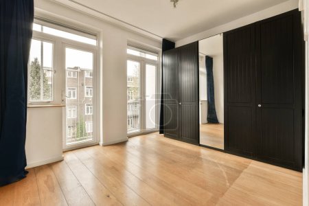 Photo for An empty room with wood flooring and black closets on either side of the room, looking out onto the street - Royalty Free Image