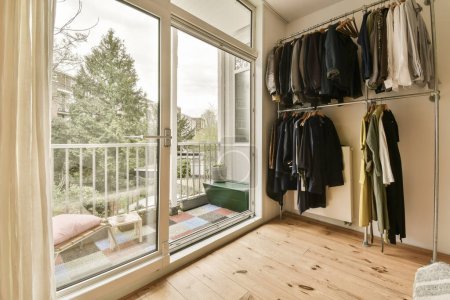 una habitación con ropa colgada en la pared y puerta corredera de cristal que conduce a un patio exterior que tiene suelo de madera