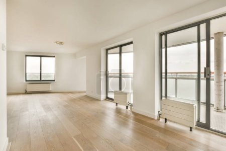 ein leeres Wohnzimmer mit Holzböden und Glasschiebetüren, die sich zum Balkon mit Blick auf das Wasser öffnen