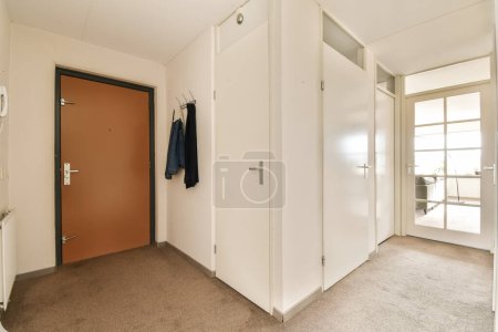 Photo for An empty room with closets and clothes hanging on the wall, in front of a red door that is open - Royalty Free Image