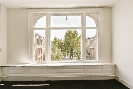 Téléchargez les photos : Une chambre vide avec une grande fenêtre et quelques arbres dans le coin, donnant sur la rue ci-dessous par une journée ensoleillée - en image libre de droit