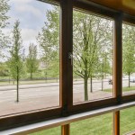 An outside view from inside a train car looking out onto the street with trees and buildings in the back ground