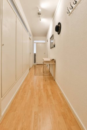 Photo for A long hallway with white walls and wood flooring on the right side, there is a tv mounted in the wall - Royalty Free Image