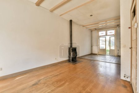 Foto de Una sala de estar vacía con suelo de madera y una estufa de leña en la parte media de la habitación son paredes blancas - Imagen libre de derechos