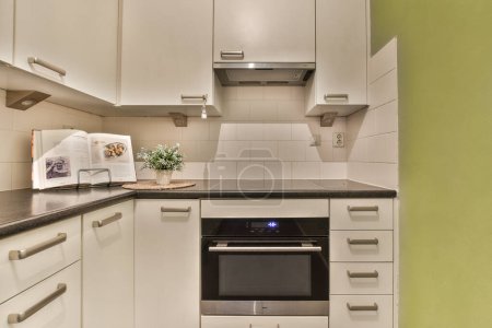 Foto de Una cocina con armarios blancos y encimeras negras en la pared encima de ella es un horno en la esquina - Imagen libre de derechos